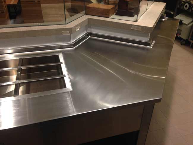 Stainless steel restaurant counter built to wrap around low walls and welded in place